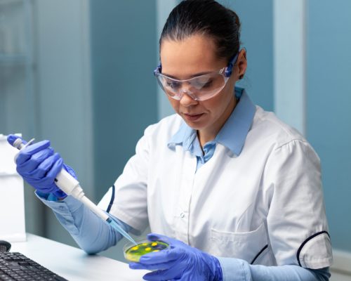 Biochemist researcher woman dropping liquid in petri dish with colony fungi using medical micropippete during microbiology experiment. Scientist doctor working in biochemistry hospital laboratory